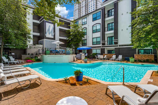 A pool area with chairs and a building in the background. at Montecito Apartments, Houston, 77056