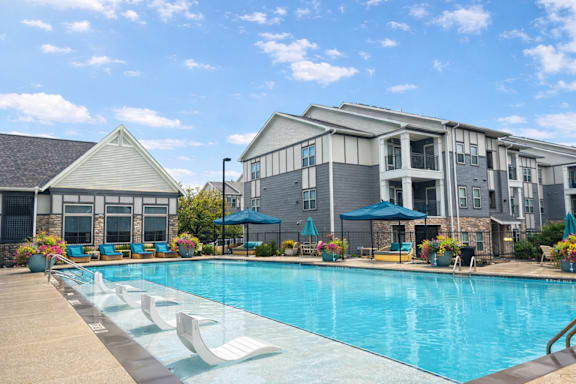 A swimming pool surrounded by lounge chairs and umbrellas in front of a building.