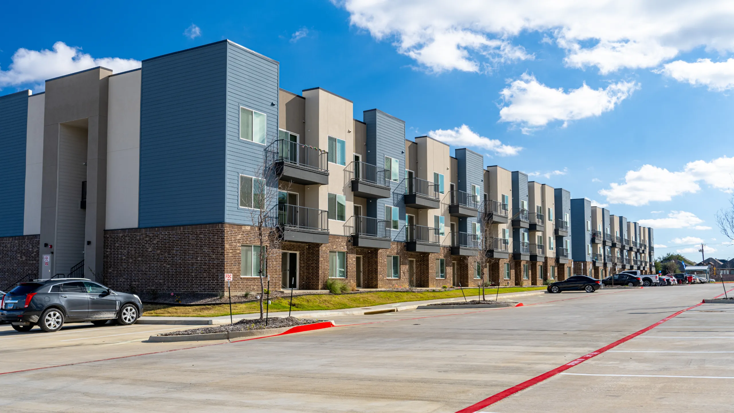 Modern apartment complex with stylish balconies and brick accents under a vibrant blue sky.