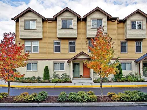 Apartments for Rent in Kenmore WA - Northshore Townhomes - Property Exterior Surrounded by Trees, with Street View, Featuring Brightly-Colored Doors, Tan and Yellow Walls, Brown Trim, and Multiple Sto