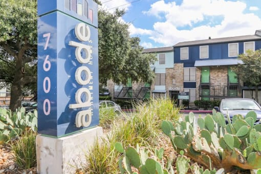 a sign in front of an apartment building with cacti and a parking lot