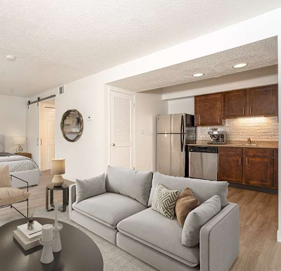 A modern living room with a grey couch and a bed in the background. at AVIA Lofts on Victors Way, Ann Arbor, MI