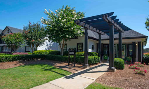 A building with a covered walkway entrance surrounded by greenery at The Madison Apartments and Townhomes, Lawrenceville, GA