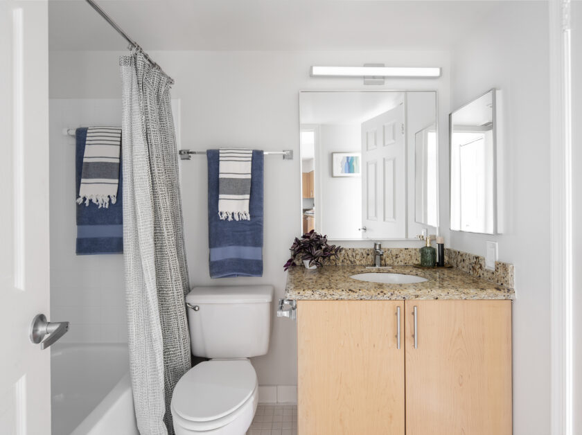 A white bathroom with a granite countertop, modern finishes and a large mirror over the sink.