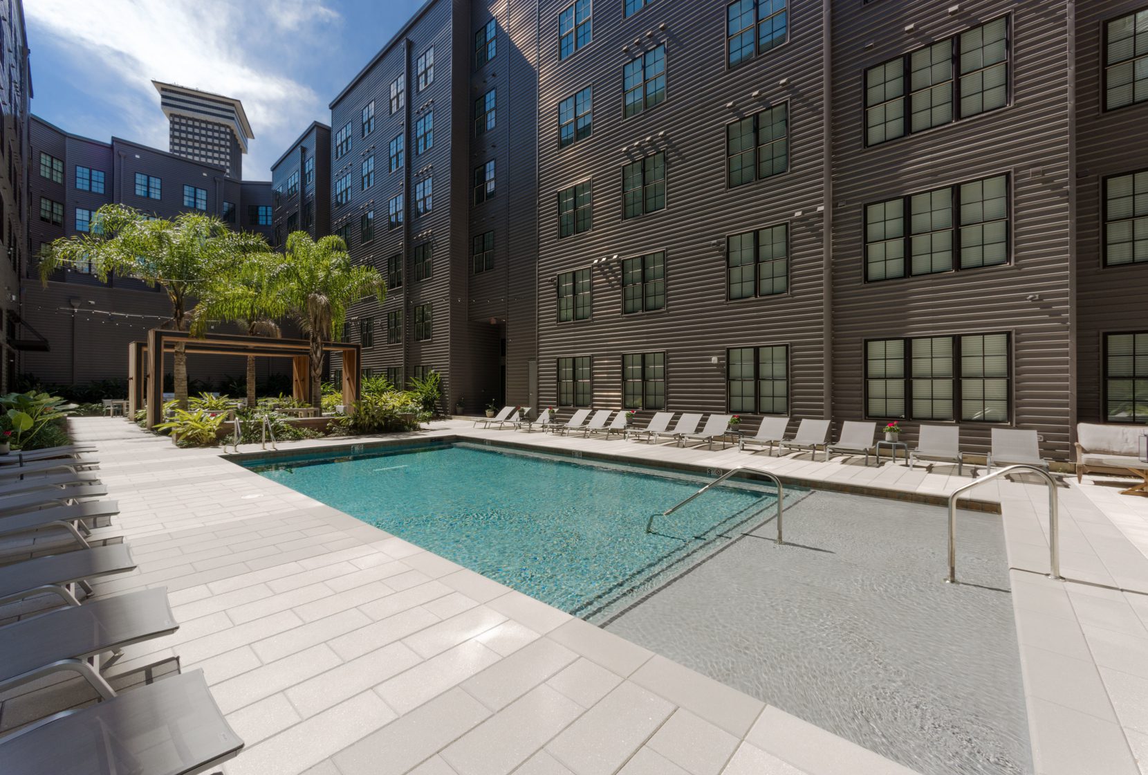 A large swimming pool with a soaking deck, surrounded by pool chaises, adjacent to a landscaped courtyard space at Paramount