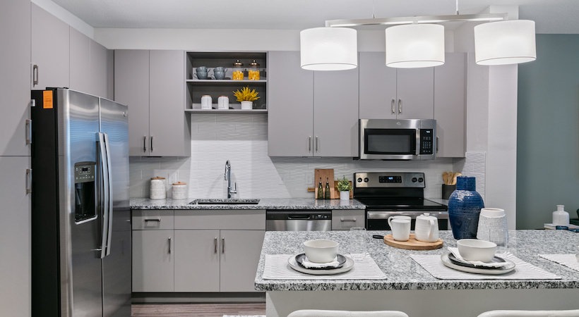 Middleburg, FL, Luxury Apartments Near Jacksonville - Integra Park at Oakleaf - Kitchen With Granite Countertops, Gray Cabinets, Stainless Steel Appliances, Tile Backsplash, And Pendant Lights.