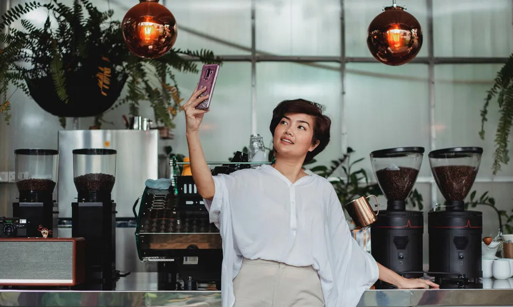 woman taking selfie in front of coffee makers in coffee shop