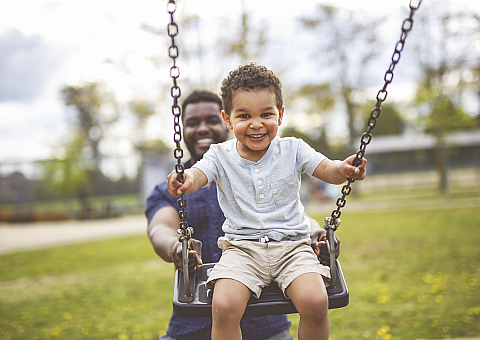 Joyful child on a swing with a parent in a sunlit park, encapsulating happiness and family moments.