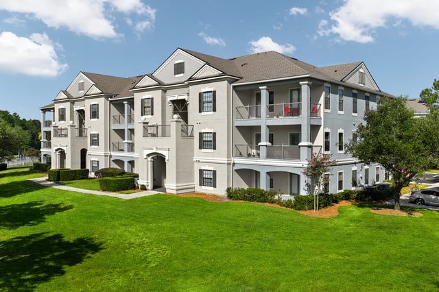 Exterior view of a multi-story apartment building with balconies and manicured lawn.
