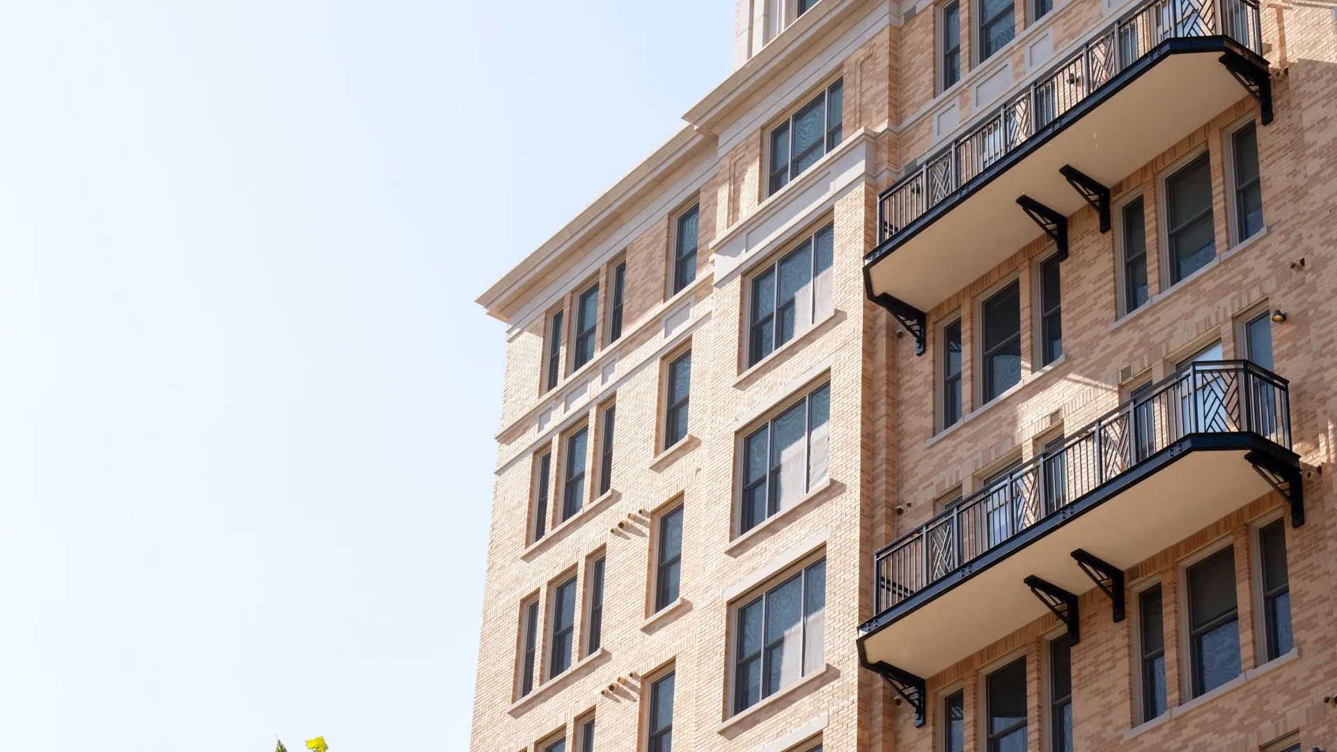 Modern brick apartment building with balconies against a clear blue sky.