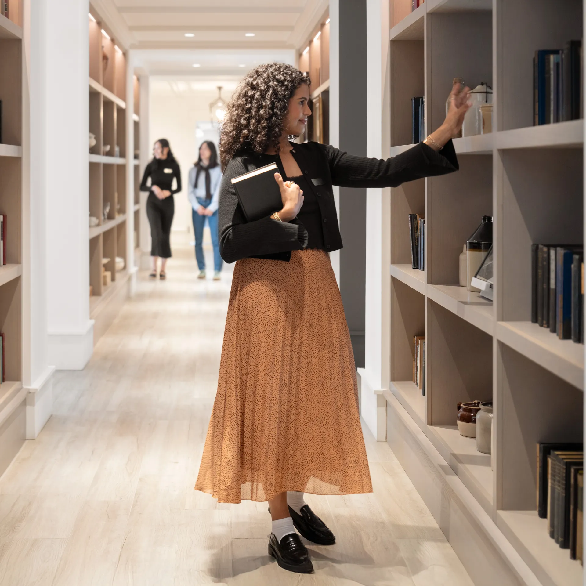 Woman browsing books in a well-lit library, with others in the background.