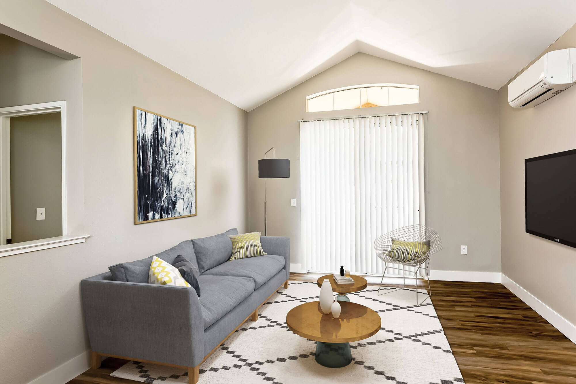 Living room at Bell Almaden in San Jose, CA with a large window and blinds, furnished with a sofa and armchair facing a television; wall-mounted air conditioning unit above the TV