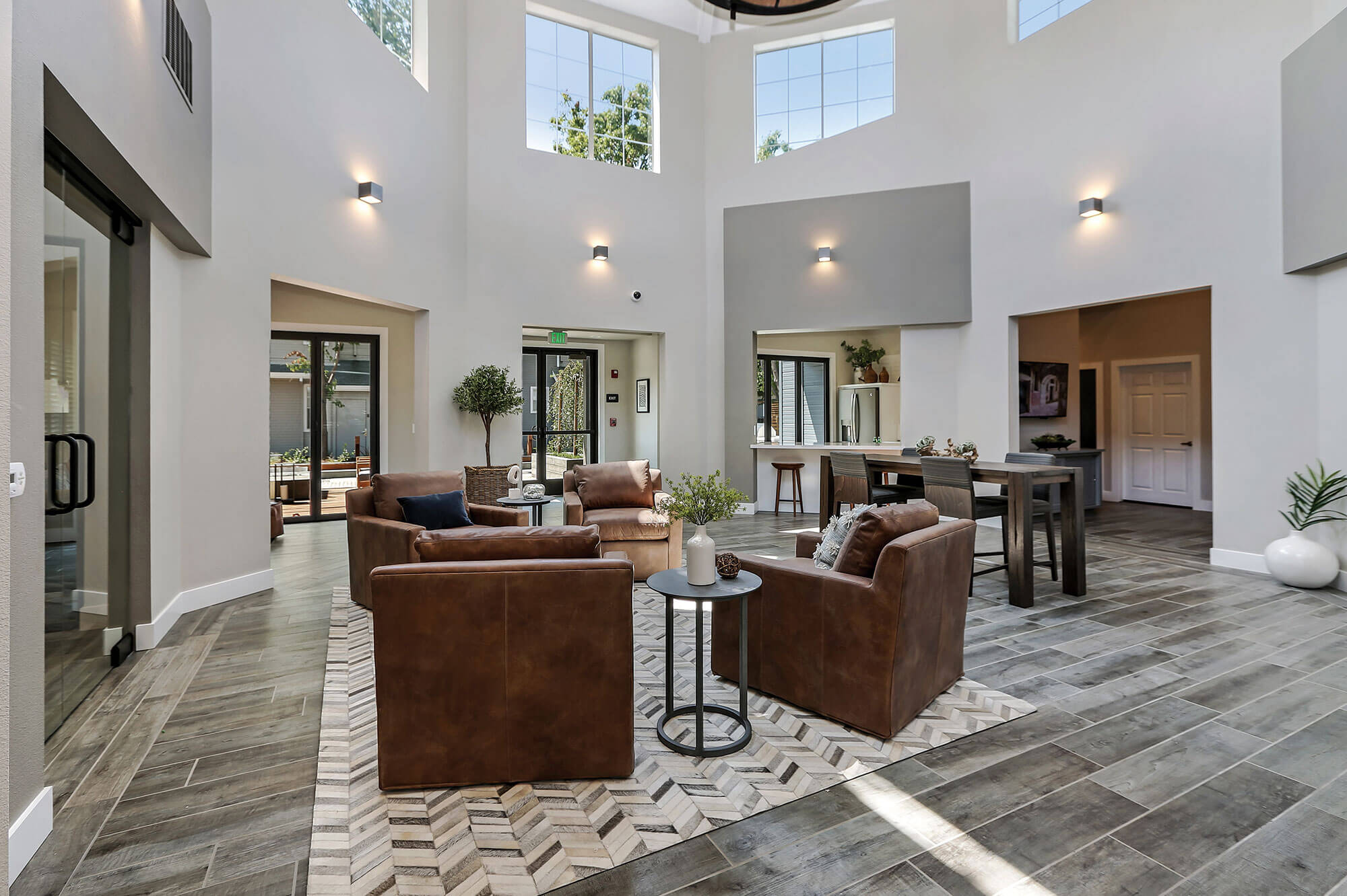 Leasing center with four armchairs and a view of the kitchen area featuring bar-height seating, with large windows at Bell Almaden in San Jose, CA