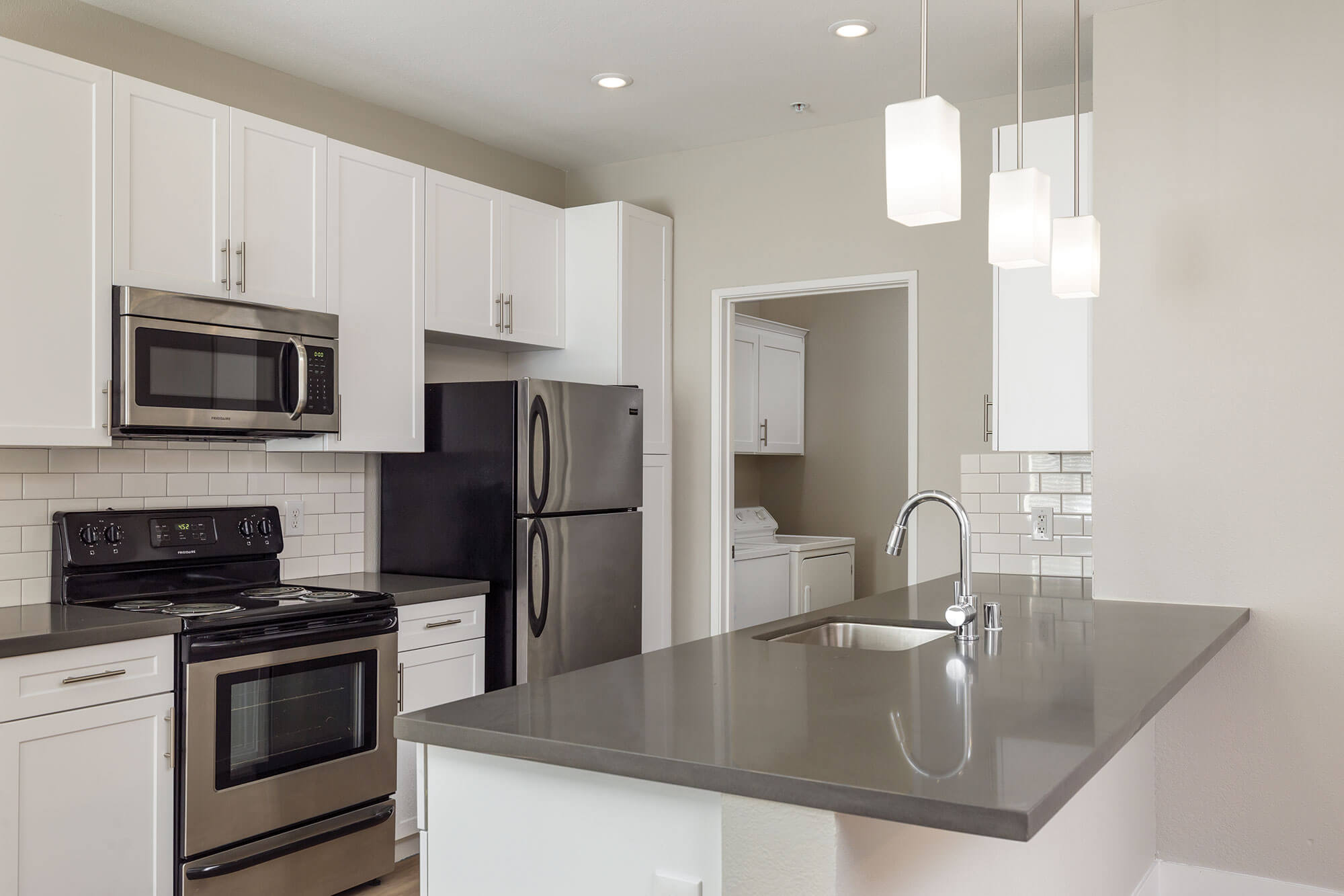 Galley-style kitchen featuring stainless steel appliances, white cabinetry, grey countertops, and white tile backsplash at Bell Almaden in San Jose, CA