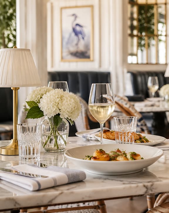 A dining table set for a meal with a plate of food and glasses of wine.