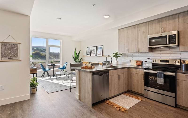 Spacious and well lit kitchen with wood floors and stainless steel appliances. 