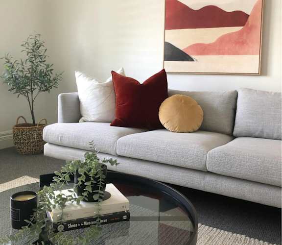A living room with a grey couch, a glass coffee table, and a framed artwork on the wall.