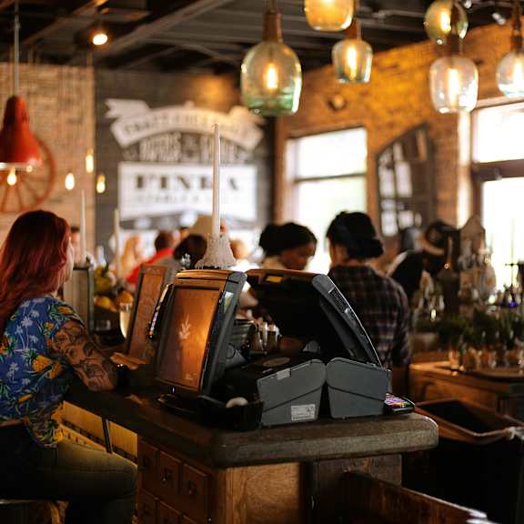 A woman with red hair is sitting at a bar with a cash register in front of her.