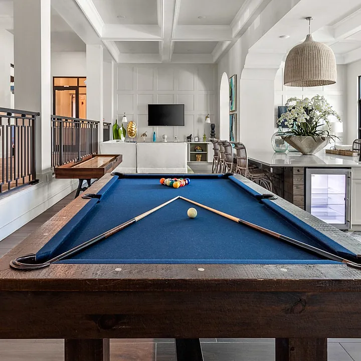 Elegant open-concept living space featuring a stylish blue felt pool table, modern bar area, and chic interior design accents.