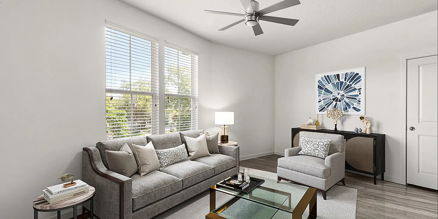 Bright and sophisticated living room featuring a plush gray sofa, elegant glass coffee table, and modern ceiling fan, enhanced by large windows with ample natural light.