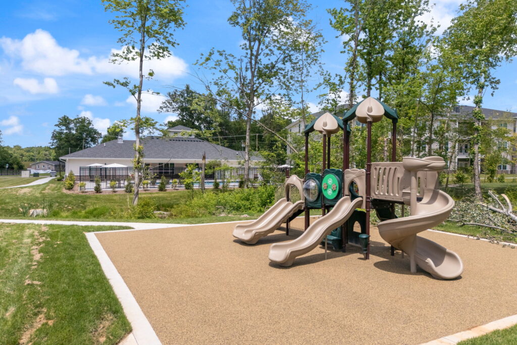 A modern playground with three slides surrounded by freshly mown grass and greenery.