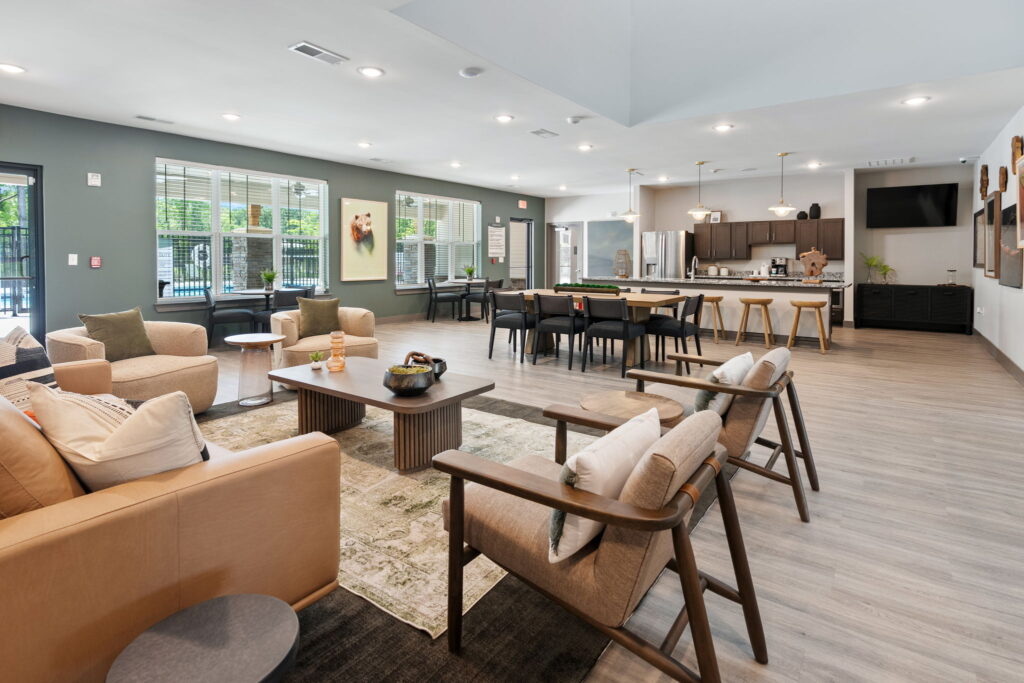 A modern community room with ample seating and natural light. There is a shared kitchen space.