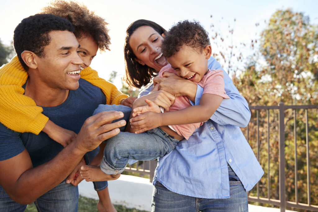 Young mixed race parents playing outdoors carrying their children in the garden