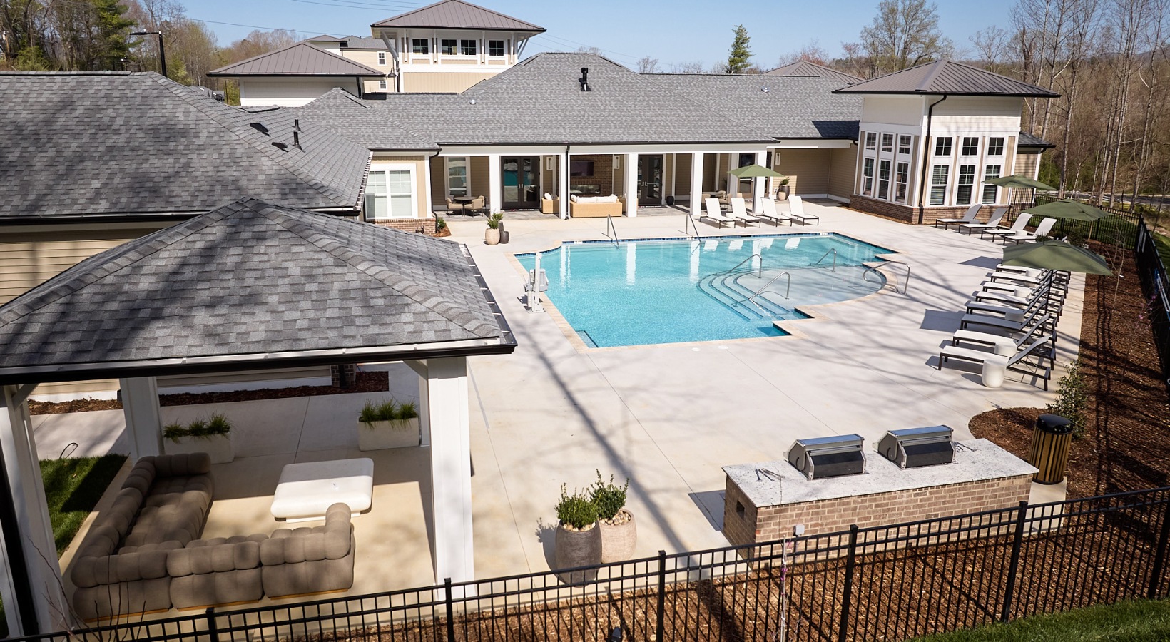 Aerial view of a resort-style swimming pool with lounge seating, covered patio, and outdoor grilling stations at a modern apartment community