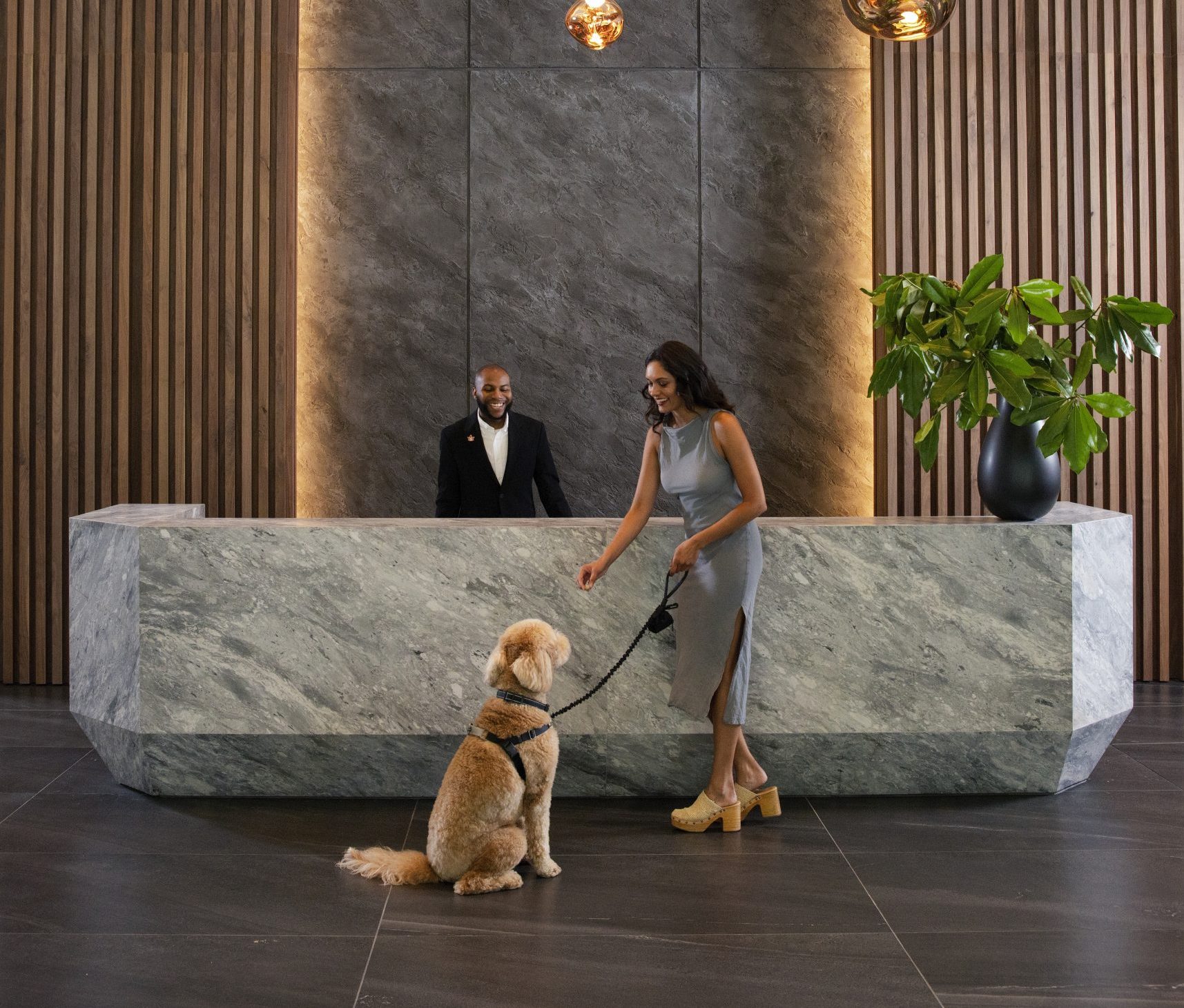 Woman with a dog standing at a modern reception desk in a lobby.