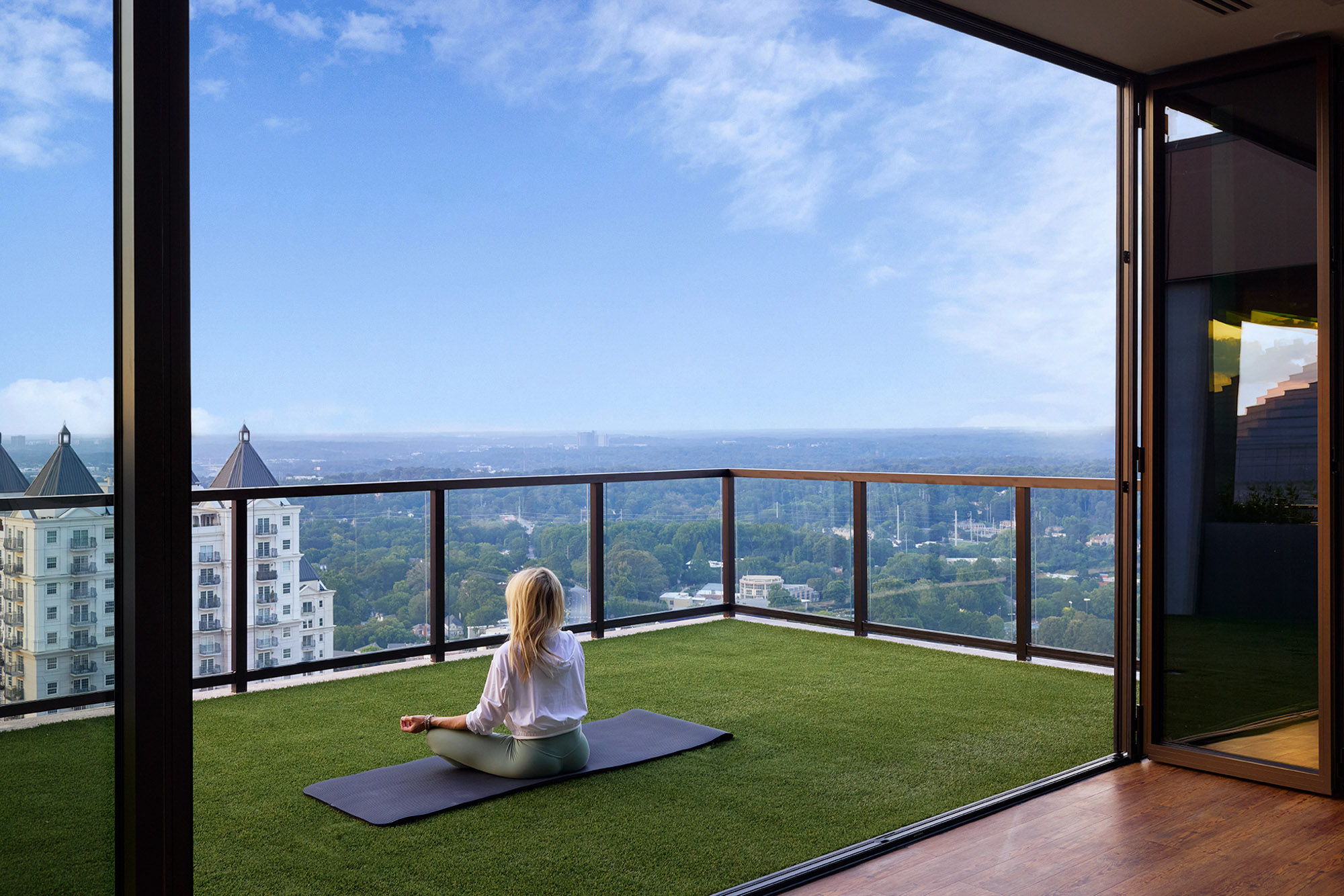 Woman seated on a yoga mat on therooftop apartment balcony
