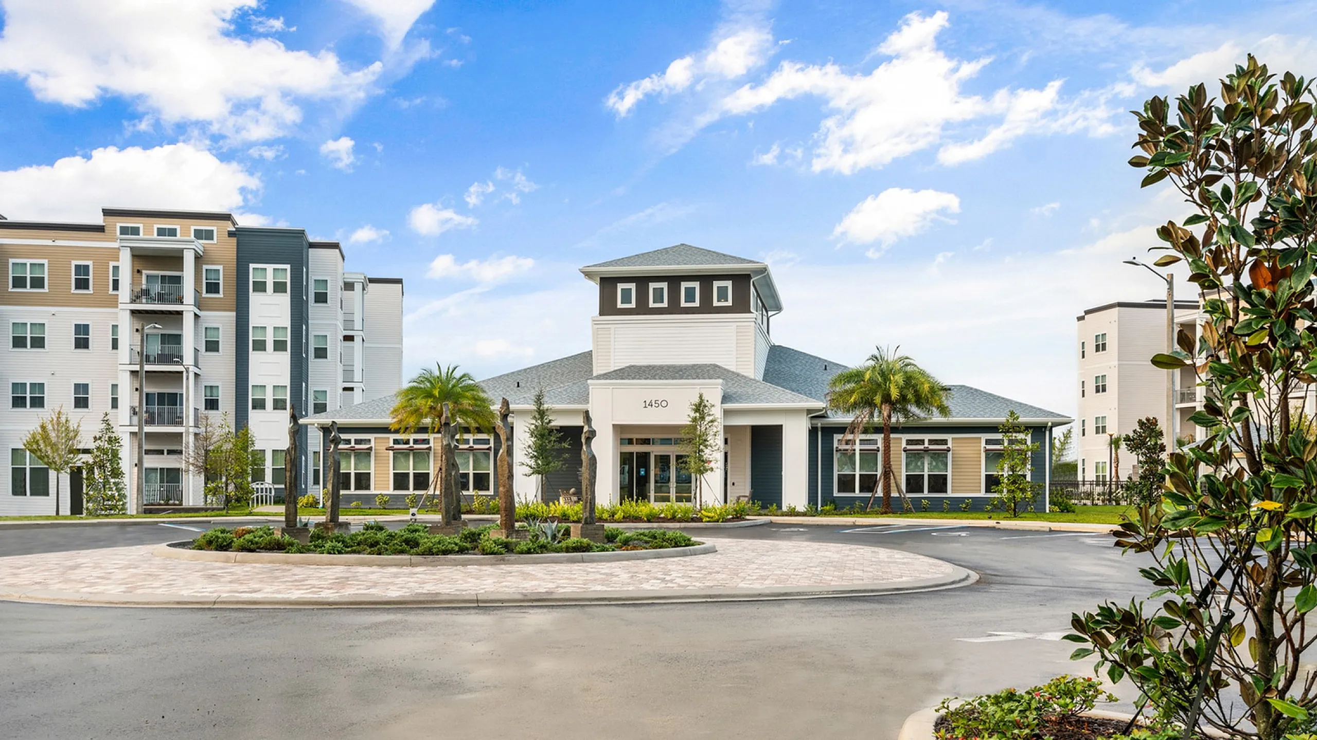 Elegant apartment complex with modern architecture, surrounded by lush landscaping and vibrant palm trees under a clear blue sky.