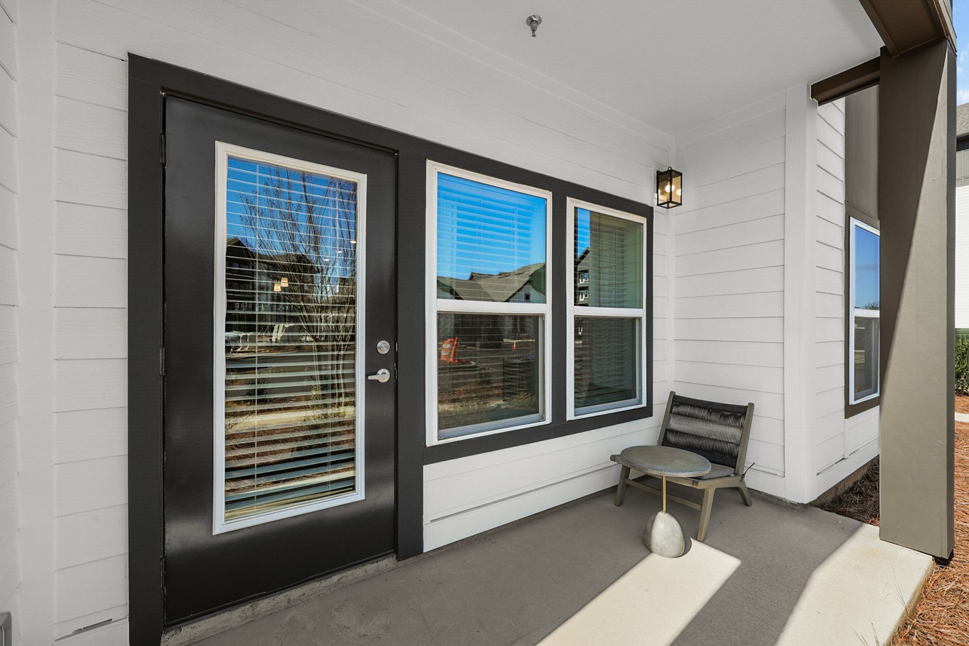 Front porch with black door, white siding, windows, bench, and small table in bright daylight.
