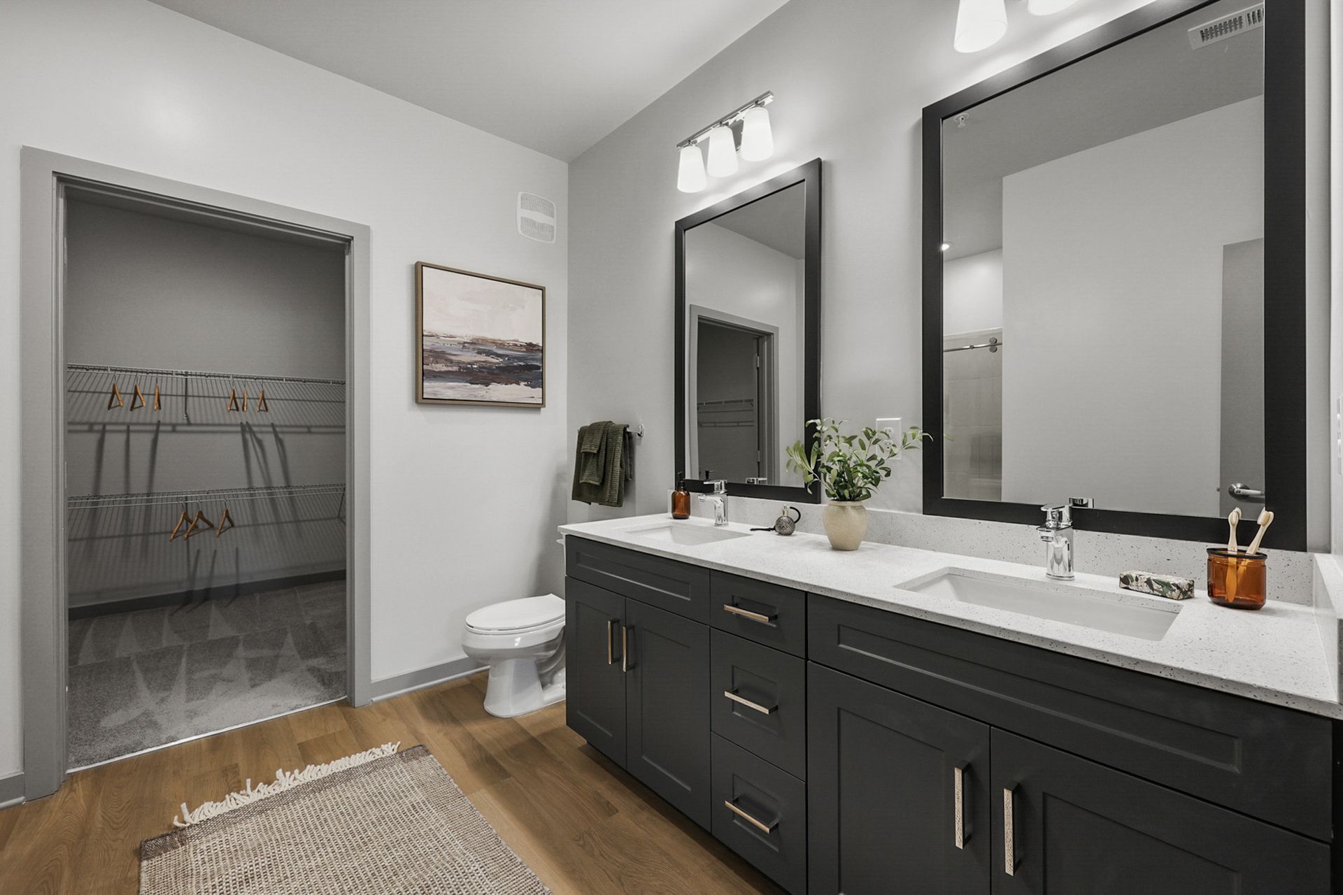 Modern bathroom with dark vanity, large mirror, white countertop, and open closet doorway