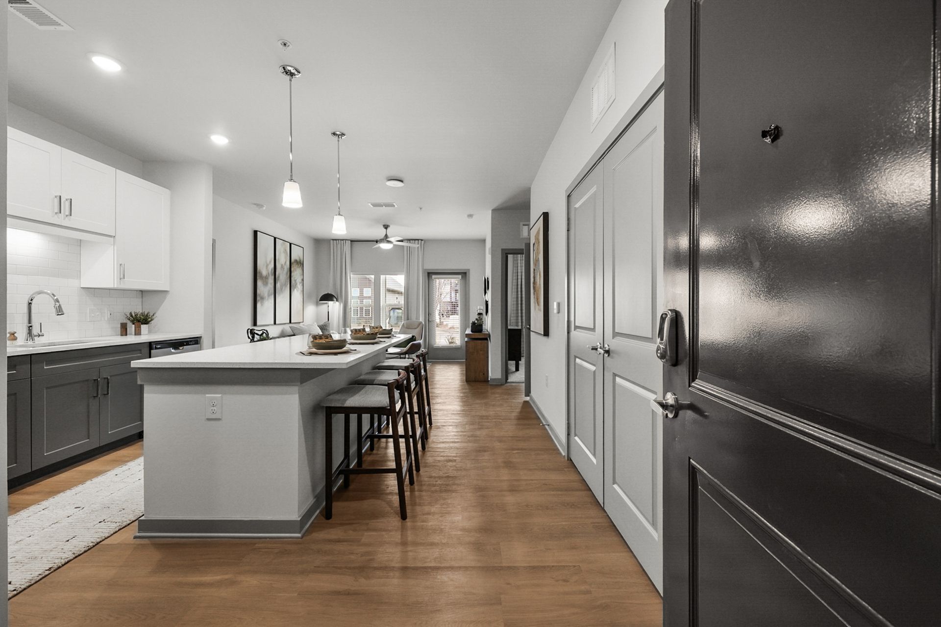 Modern open-concept kitchen with gray island, wood floors, and black front door