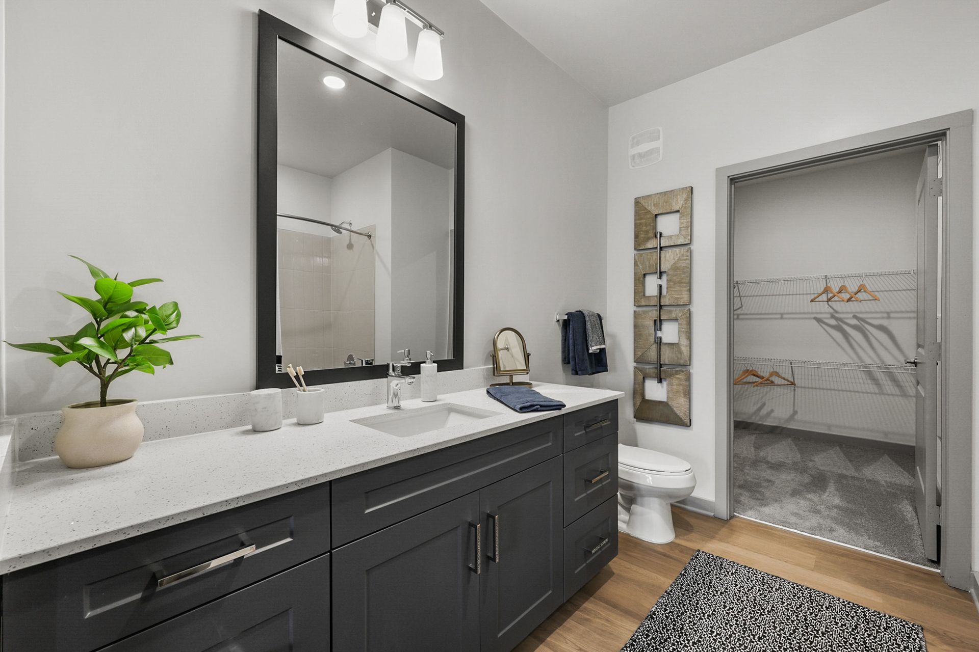 Modern bathroom with dark vanity, large mirror, white countertop, and open closet doorway