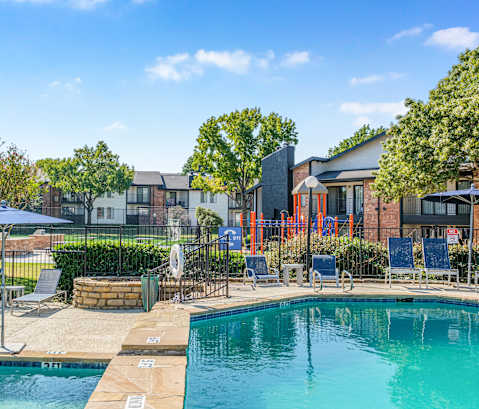 A swimming pool surrounded by lounge chairs and umbrellas with a building in the background. at Water Ridge Apartments , Texas, 75061