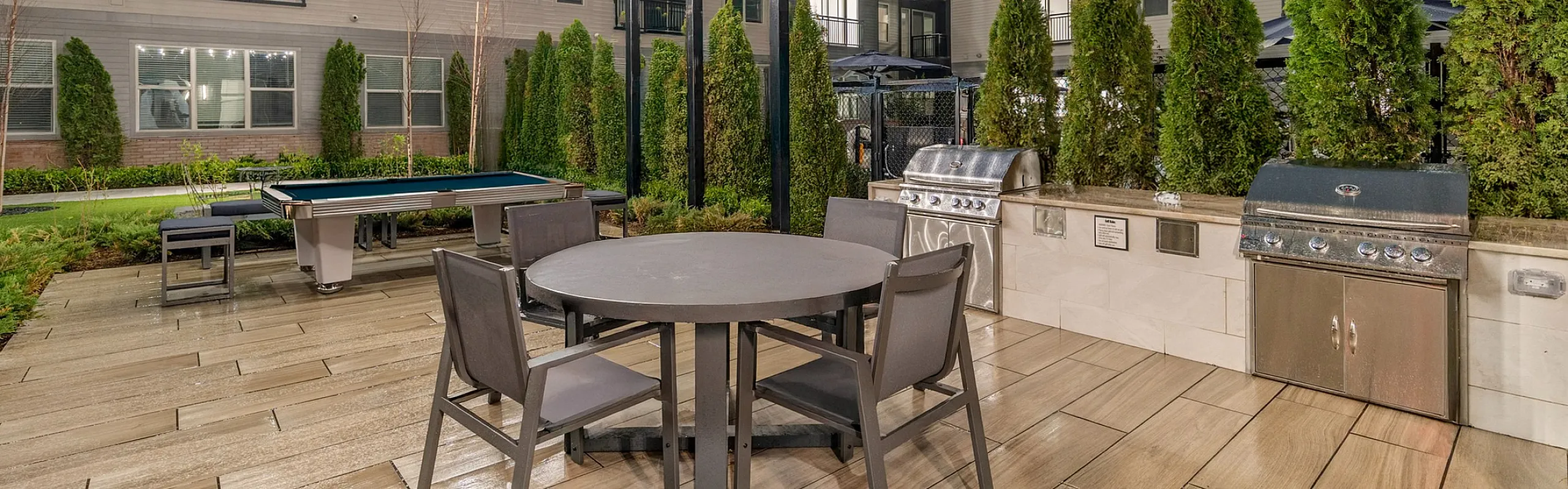Elegant outdoor patio space with dining table, BBQ grills, and stunning evening lighting, perfect for relaxation and entertainment.