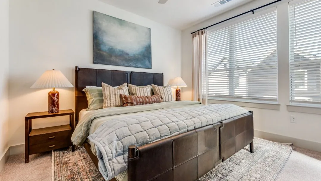A modern bedroom with a large bed, water-themed art, and bright windows.