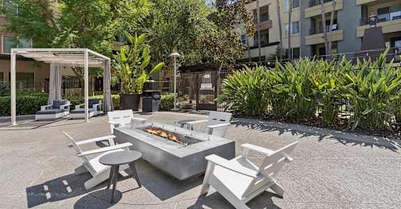 A white outdoor barbecue grill with chairs and a table is set up in a courtyard at The Kitt at Warner Center in Woodland Hills, CA, 91303