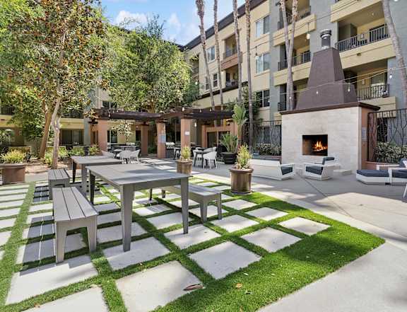 A patio with a table and chairs is surrounded by a grassy area and apartment buildings at The Kitt at Warner Center in Woodland Hills, California, 91303
