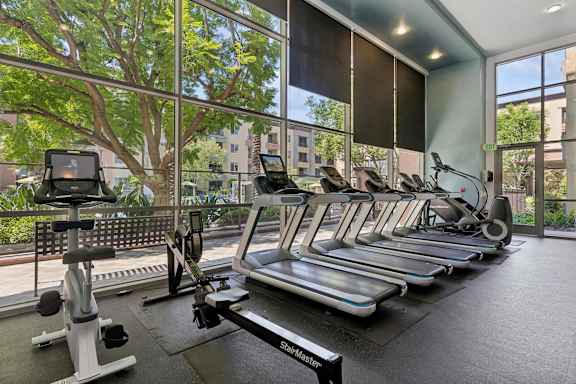 A gym with treadmills, elliptical machines, and a rowing machine. at The Kitt at Warner Center Apartments, Woodland Hills, California