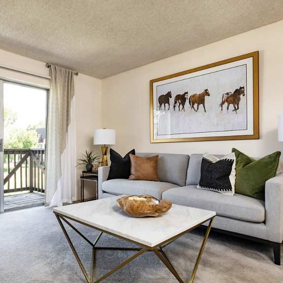 A living room with a grey couch, a green chair, and a painting of horses on the wall.