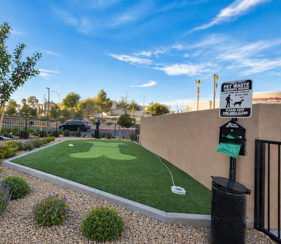 A small putting green is surrounded by a low fence and a sign that says "Pet Waste.".