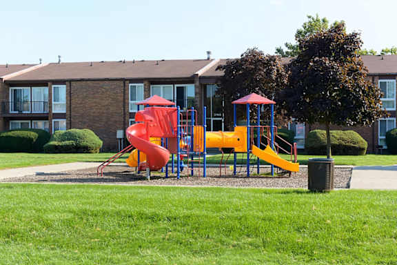 A playground with a red slide and yellow slide in front of a building.