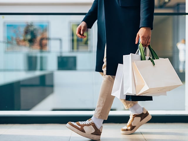 Chic shopper in a stylish coat and sneakers walking with multiple shopping bags, embodying urban elegance.
