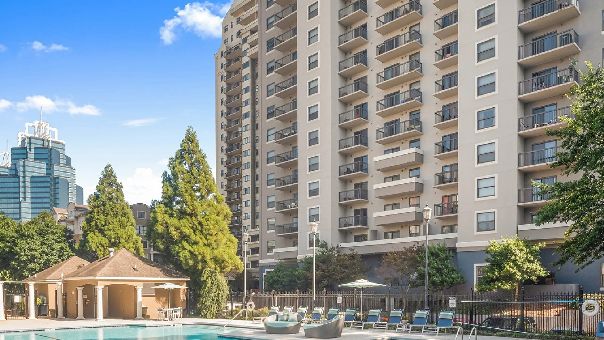Inviting apartment complex with serene outdoor pool area, surrounded by lush greenery and modern high-rise architecture.