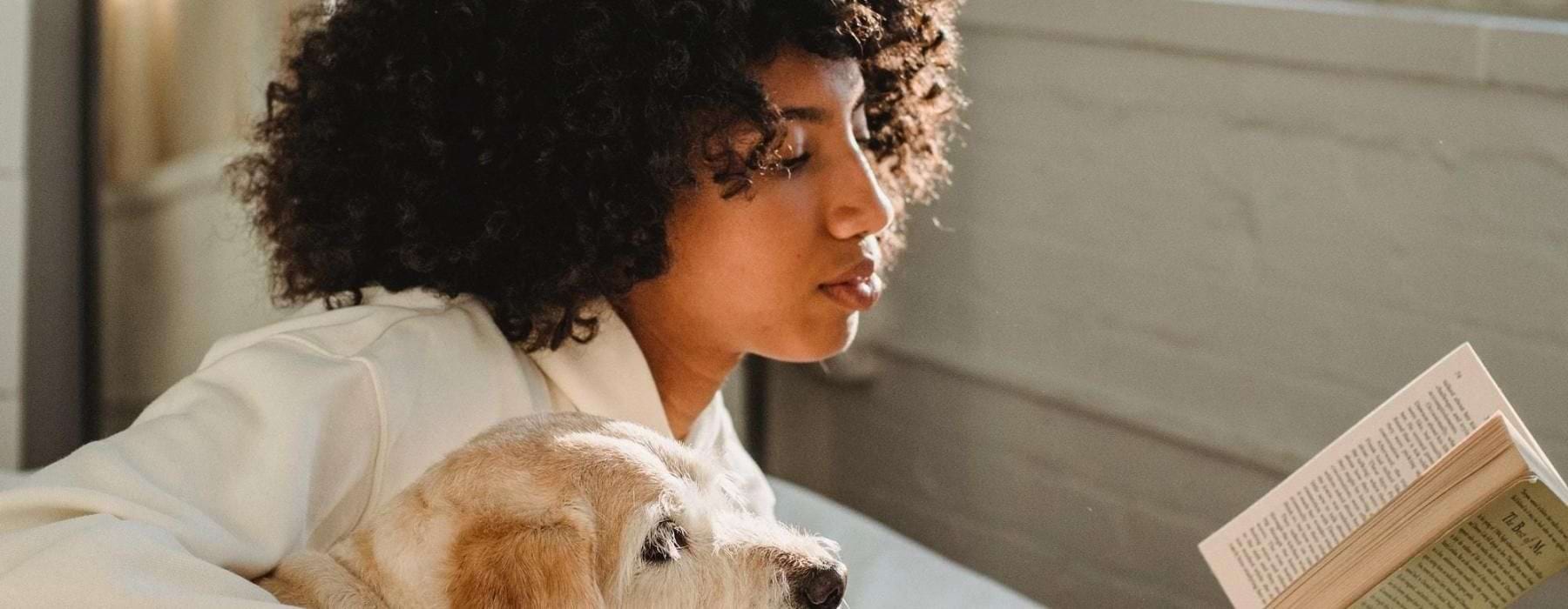 a person reading a book while laying next to a dog