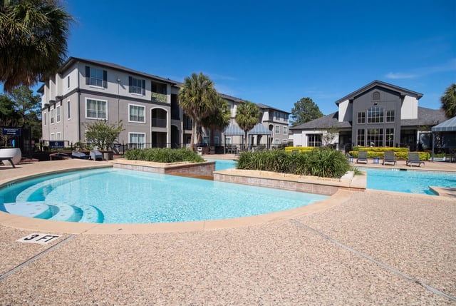 Resort-style swimming pool and lounge area with apartment buildings in the background.