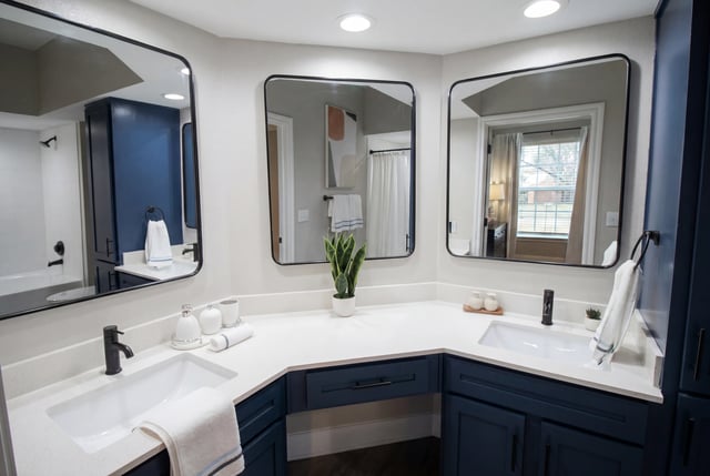 Modern bathroom with dual sinks, large mirrors, and dark blue cabinetry.