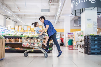 dad playing and pushing daughter in a shopping cart of grocery store